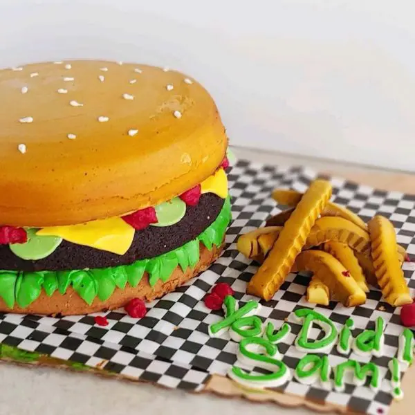 A hamburger cake and fries on a checkered table cloth.