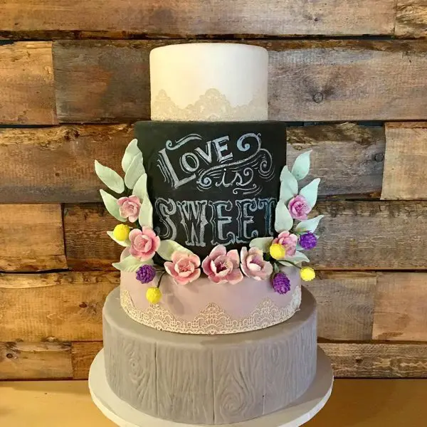 A cake with flowers and chalkboard on top of it.