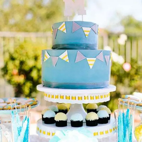 A blue cake with bunting on it and cupcakes