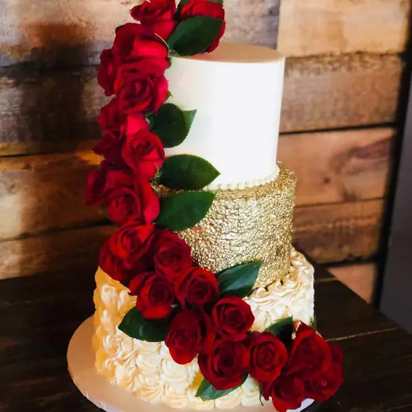 A white and gold cake with red roses on it