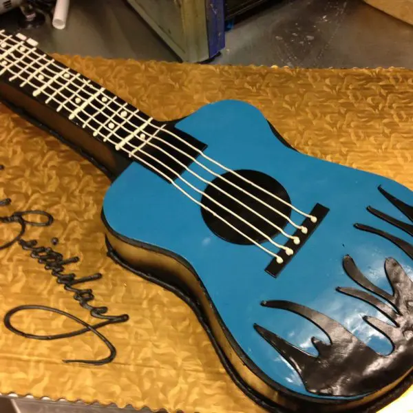 A blue guitar cake with black writing on it.