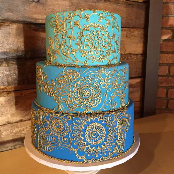 A three layer cake with gold designs on it.