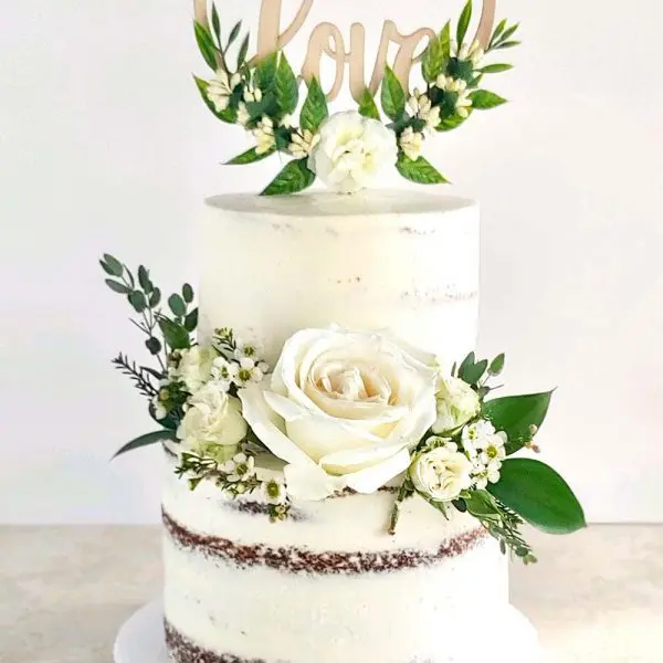 A three layer cake with flowers and greenery on top.