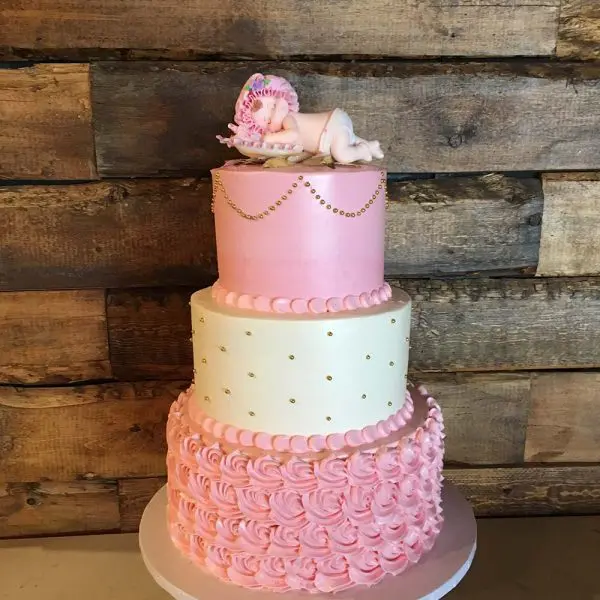 A pink and white cake with a baby carriage on top.