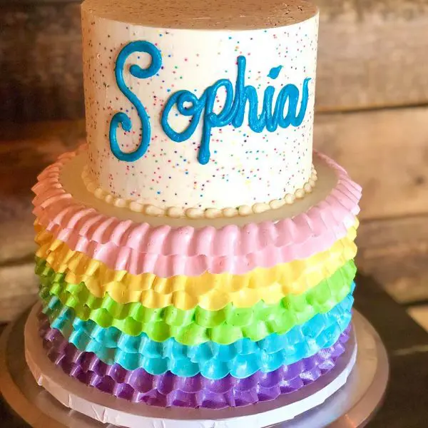 A cake with rainbow colored ruffles and name of sophia