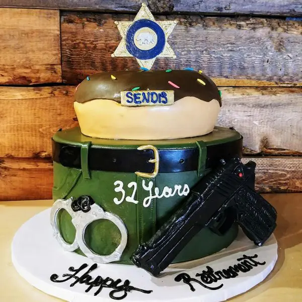 A cake with a gun, handcuffs and sheriff star on top.