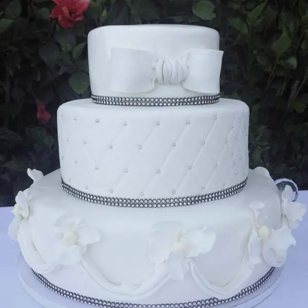 A white wedding cake with flowers and bows on top.