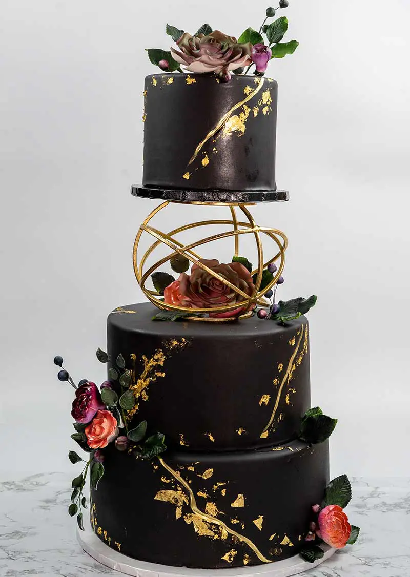 Elegant black and gold tiered cake with floral and geometric decorations.